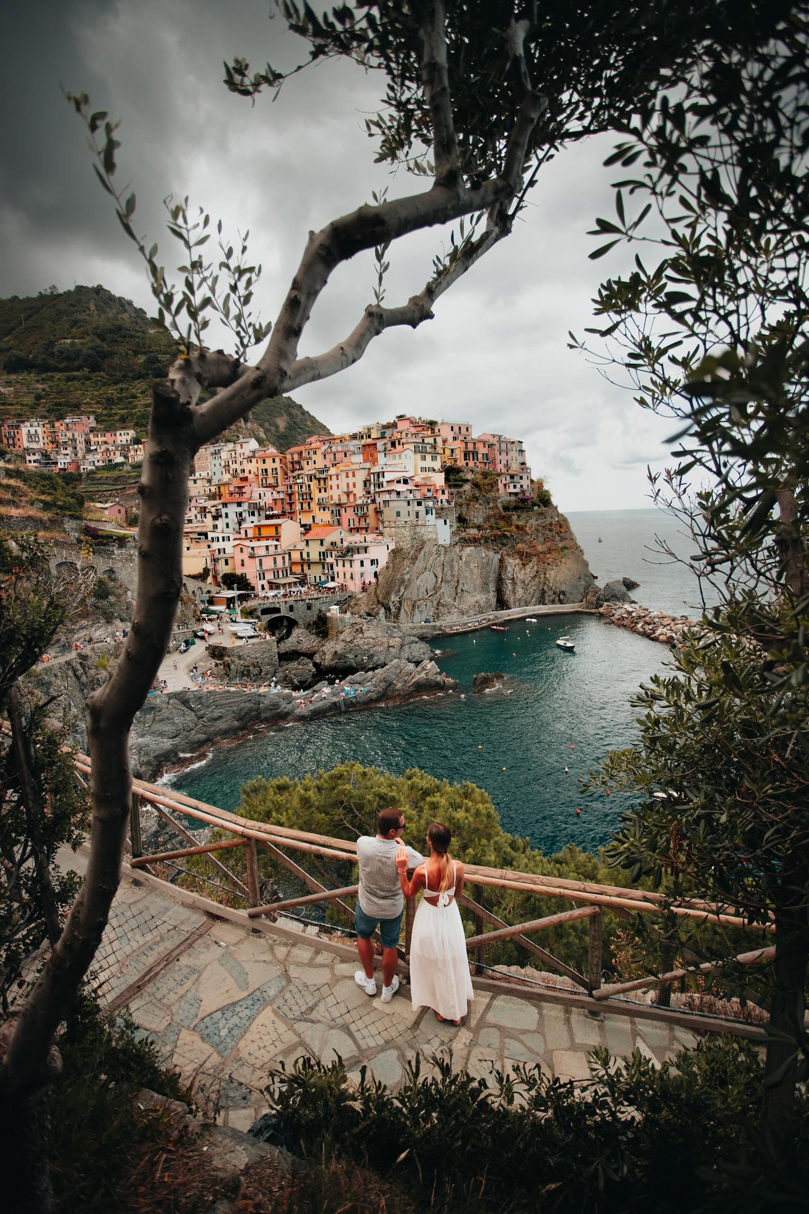 A couple stands on a scenic overlook, gazing at the colorful coastal village of Cinque Terre, Italy.